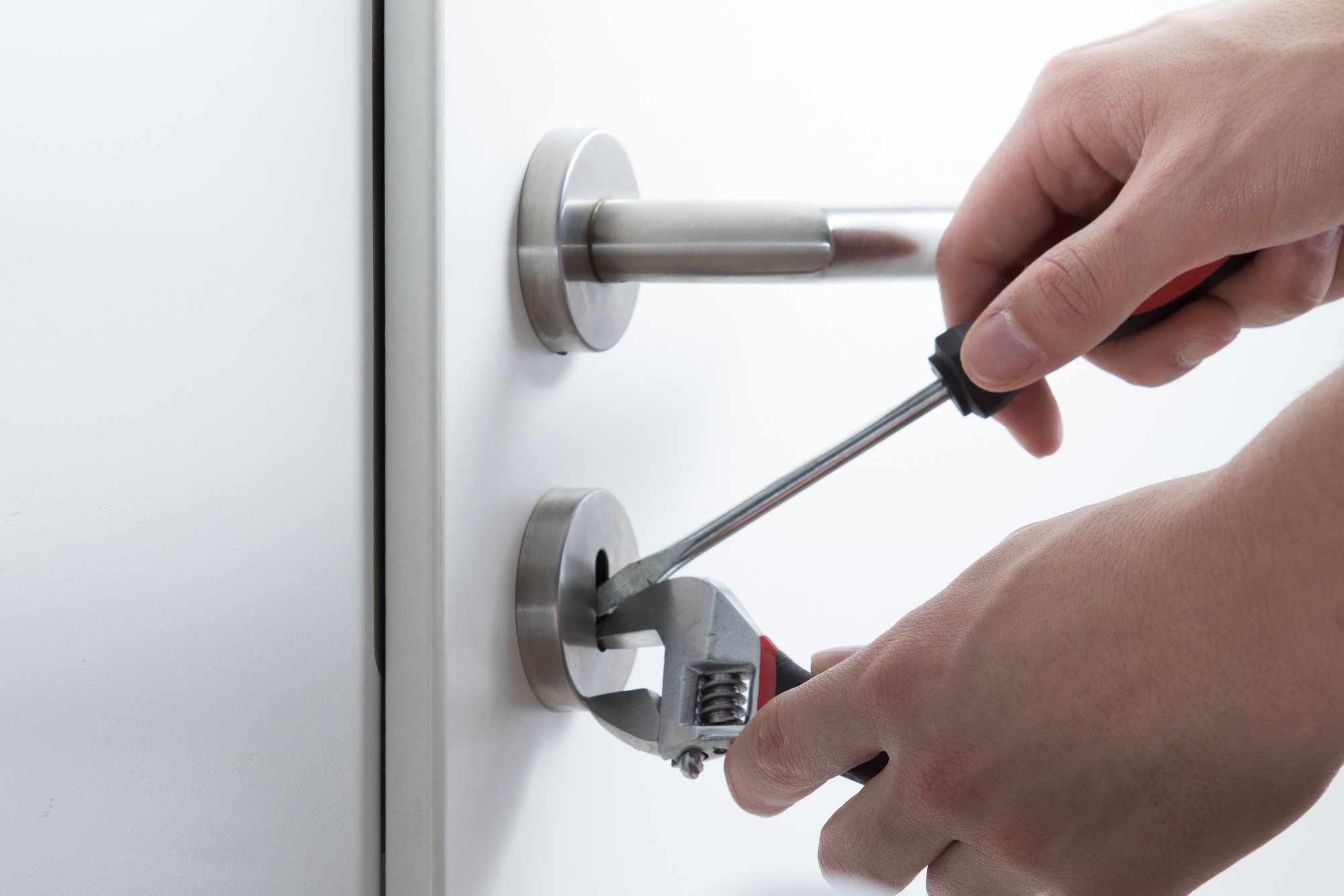 A person using pliers and a screwdriver to repair a door lock, emphasizing home maintenance and repair techniques.