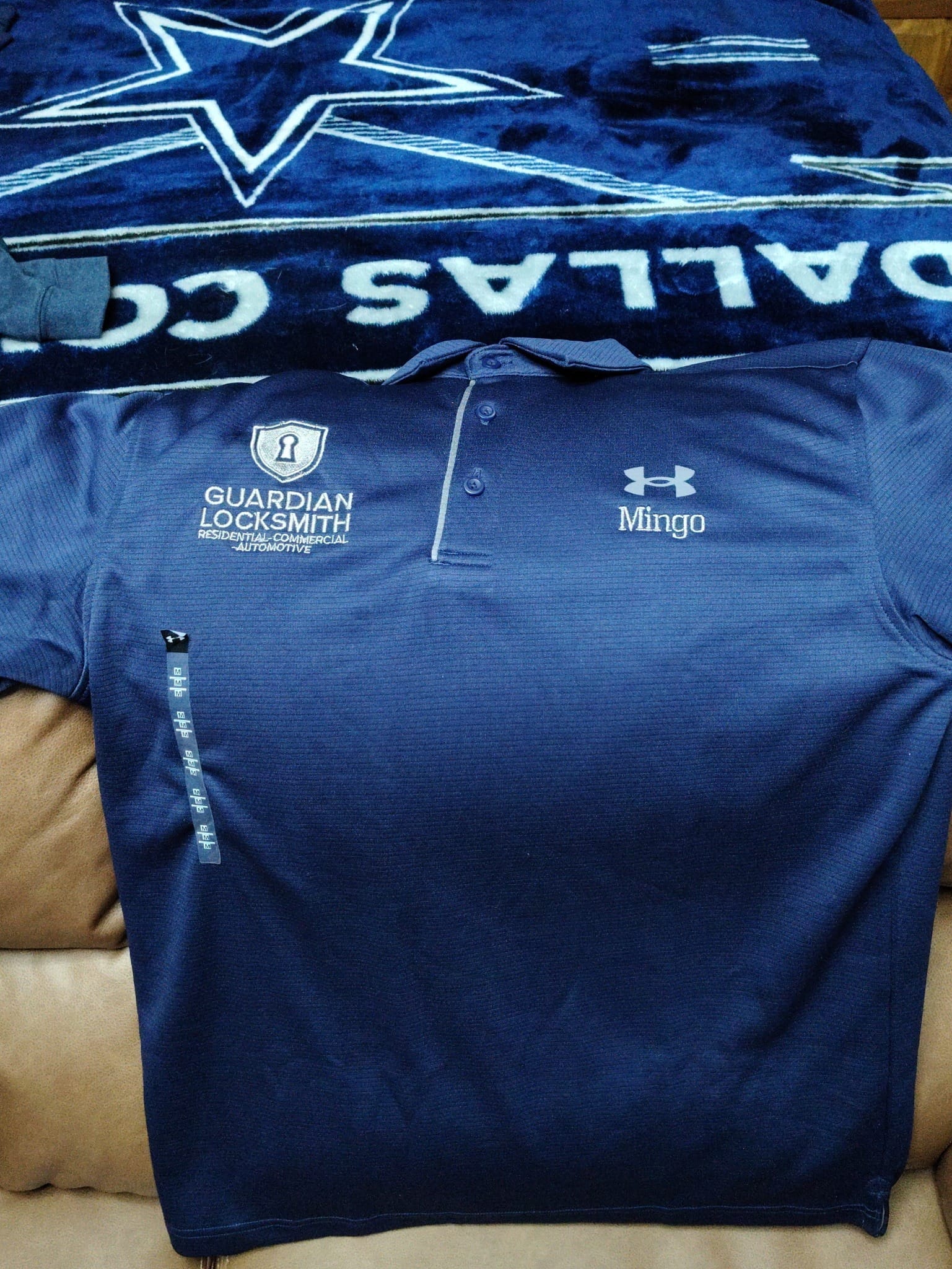 Navy polo shirt with "Guardian Locksmith" and "Mingo" logos, laid on a Dallas Cowboys blanket, highlighting branding for a locksmith service.