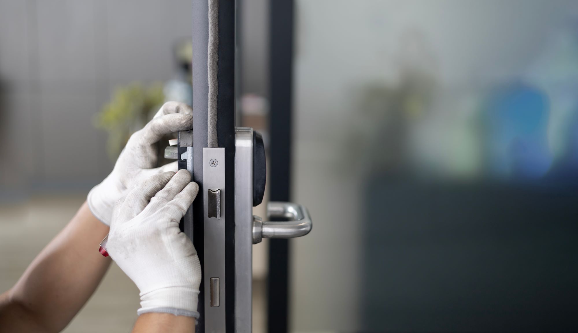 A person wearing gloves installs a door lock, focusing on the mechanism against a modern, blurred background, highlighting home security tasks.